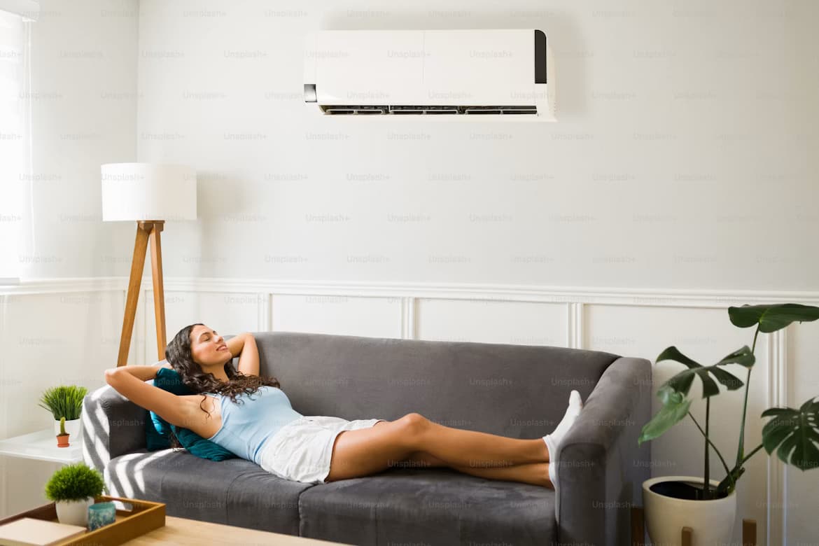 A woman relaxing on a sofa beneath a wall-mounted air conditioner