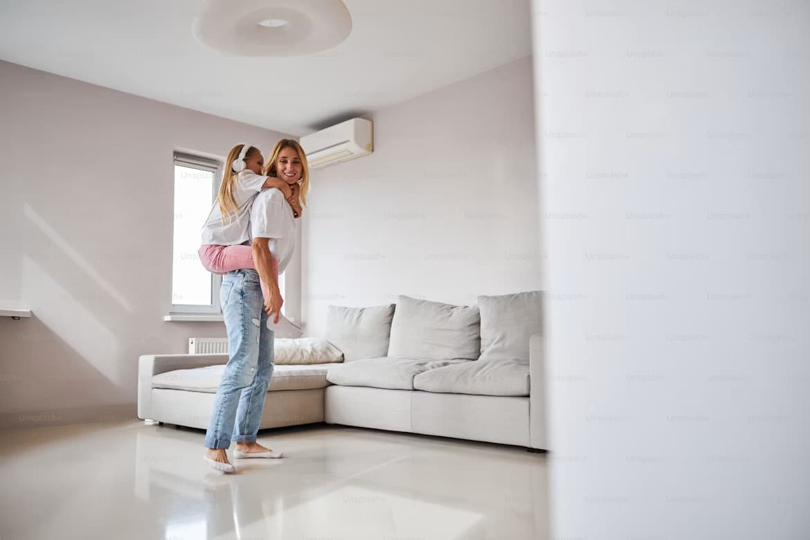 A parent and child in a bright living room cooled by a wall-mounted unit