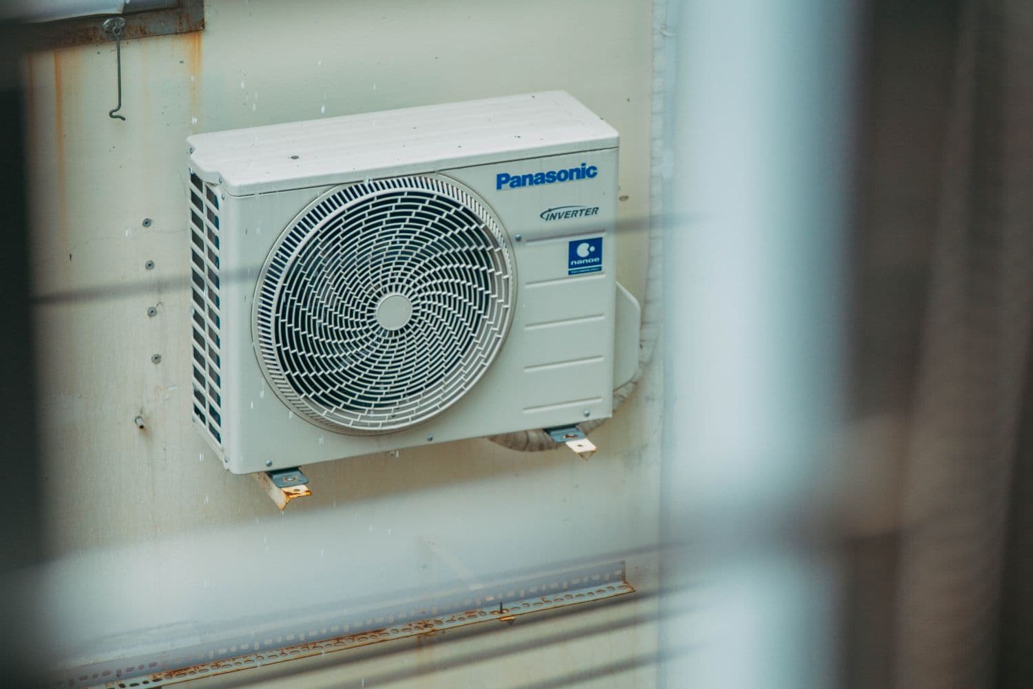 An outdoor air-conditioning condenser unit mounted beside a home